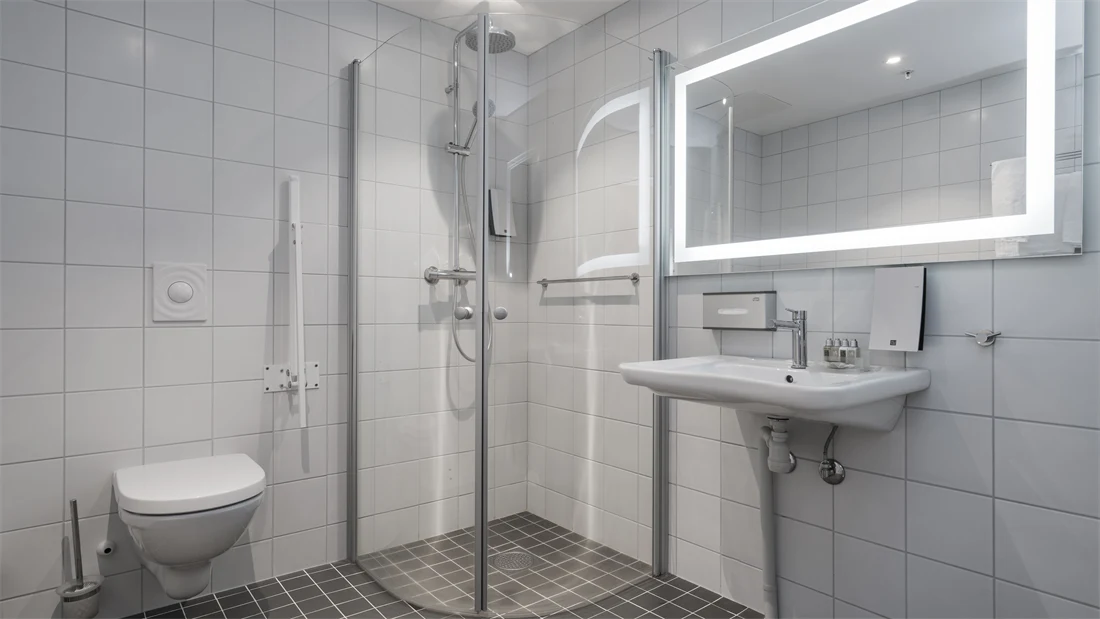 Dusj, toalett og vask med god gulvplass og støttearmer rundt toalett på  handikaprom på Thon Hotel Lofoten