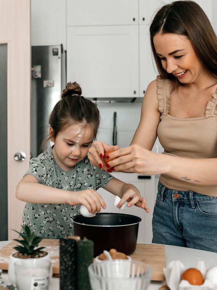 Jente baker sammen dame på kjøkkenet, diverse interiørartikler og ingredienser i uskarp forgrunn. Foto til artikkel om gavetips til farsdag.