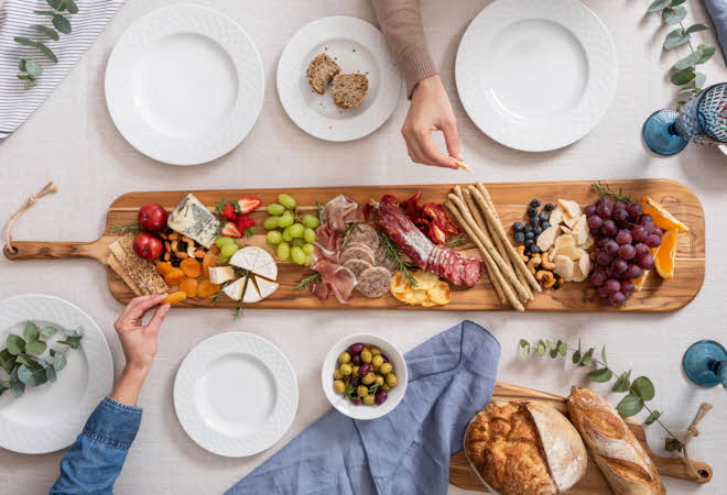 Et bugnende tapasbrett med ost, kjøtt, frukt og nøtter står midt på bordet, omgitt av tallerkener.