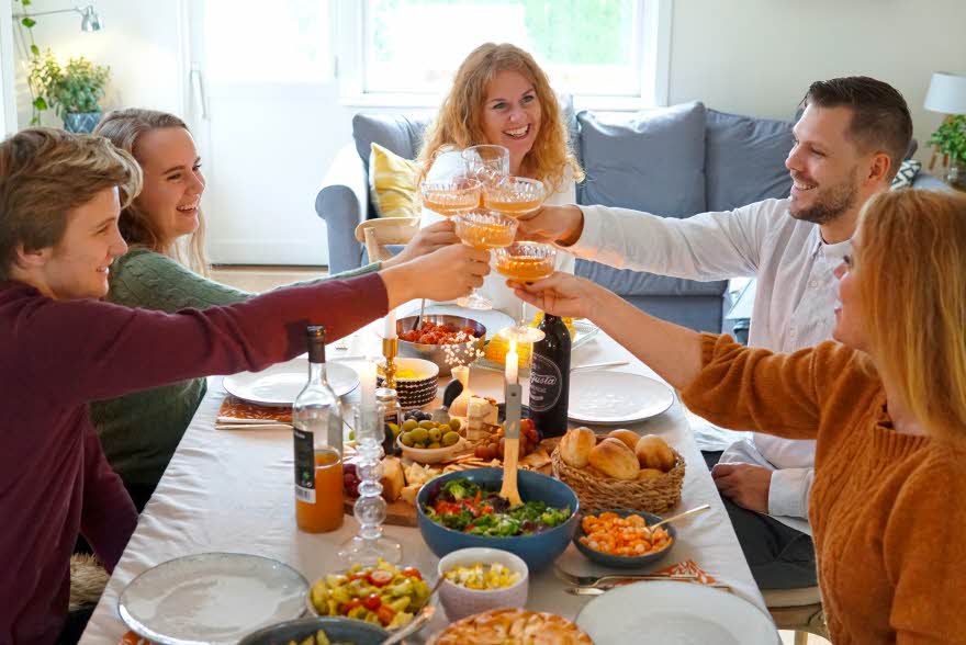 Dekket bord med mat og folk som smiler og skåler