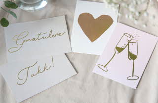 Tre gratulasjonskort på lys stoff, med ordet "Gratulerer", et gullhjerte, og to champagneglass.