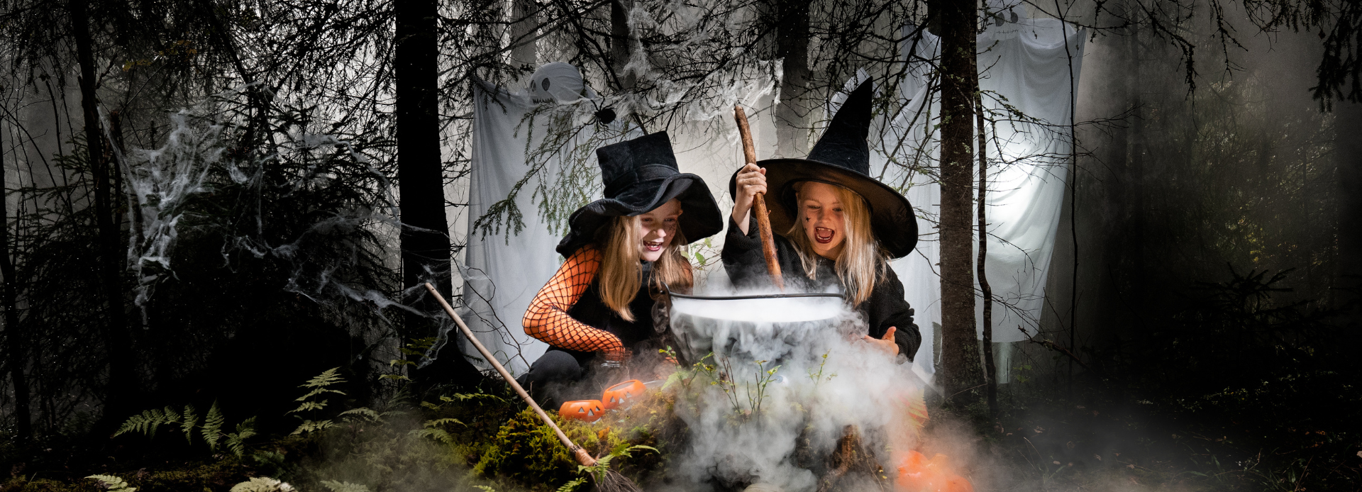 2 barn forkledd som hekser, over en gyte i morkdusk skog