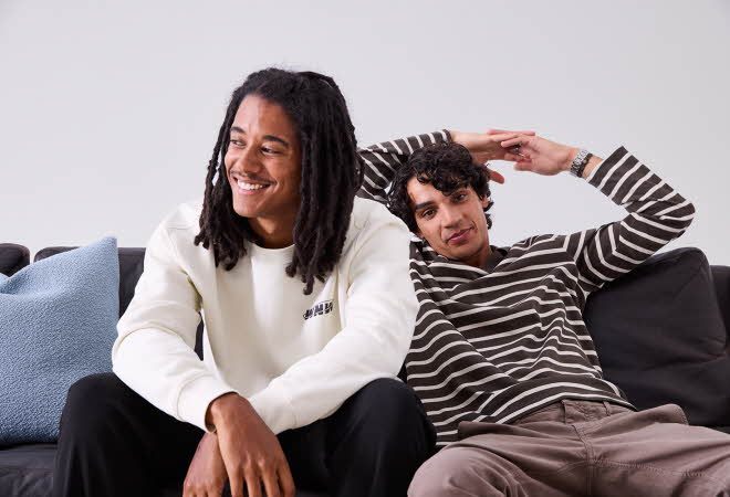 En mann i stripete genser og en mann i hvit genser sitter ved siden av hverandre på en sofa.