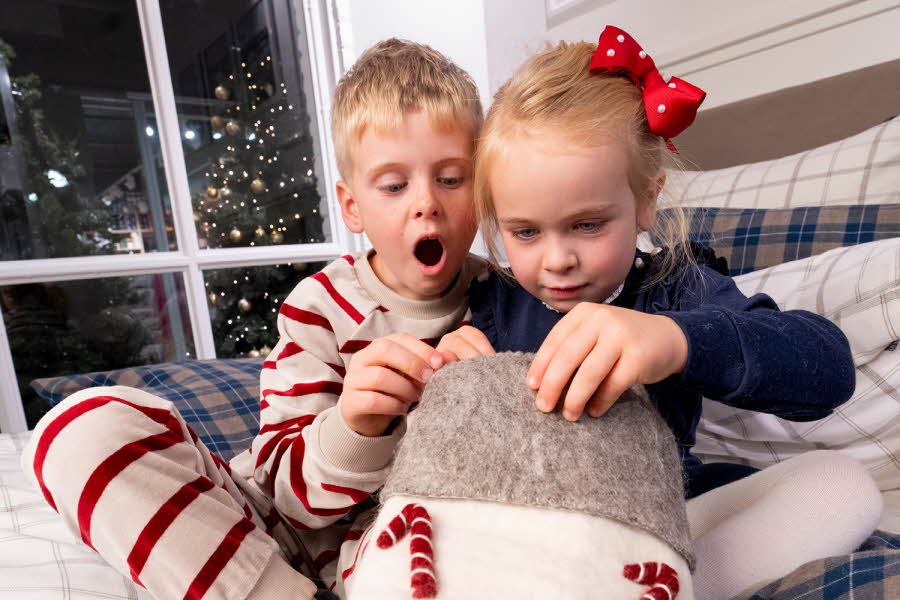 To barn sitter i seng og ser ned i en stor julestrømpe.