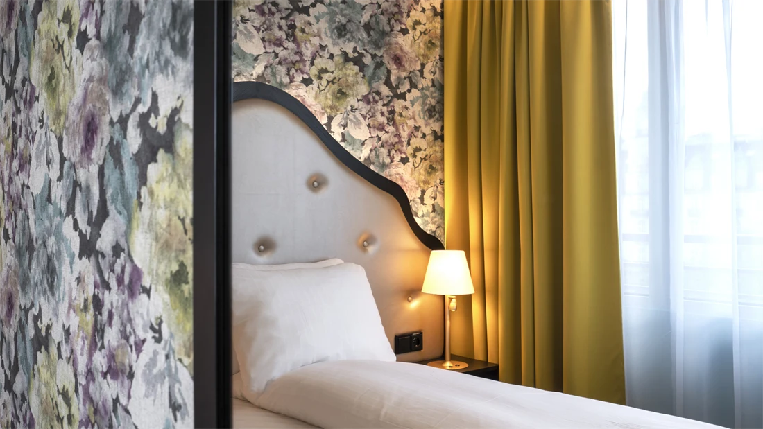 Dobbeltseng med sengegavl, blomstrete tapet og gule gardiner i dobbeltrom på Thon Hotel Cecil