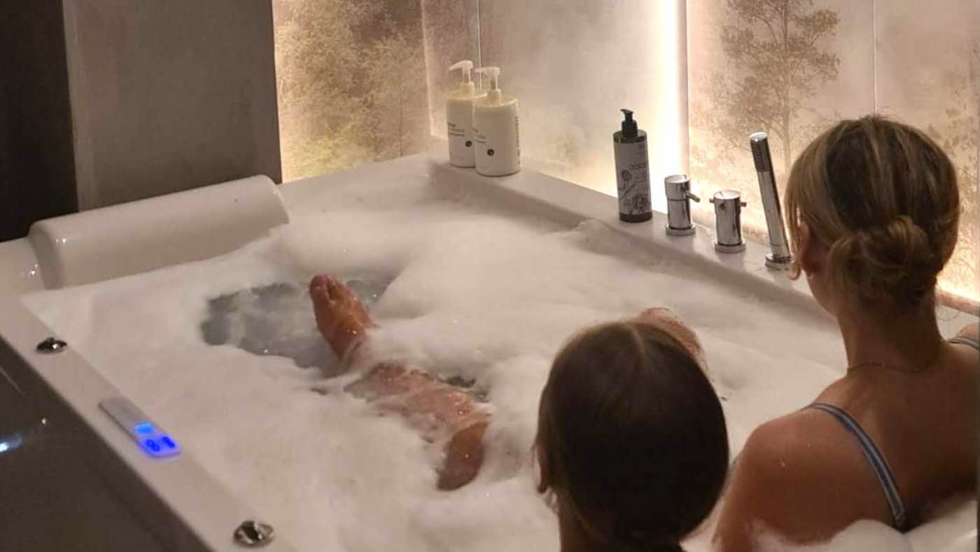 to damer sett bakfra som sitter i badekar med masse bobler