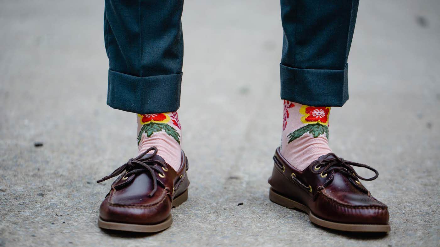 nærbilde av beina til en mann med moderne mokkasiner og rosa sokker med blomster på og oppbrettet bukse
