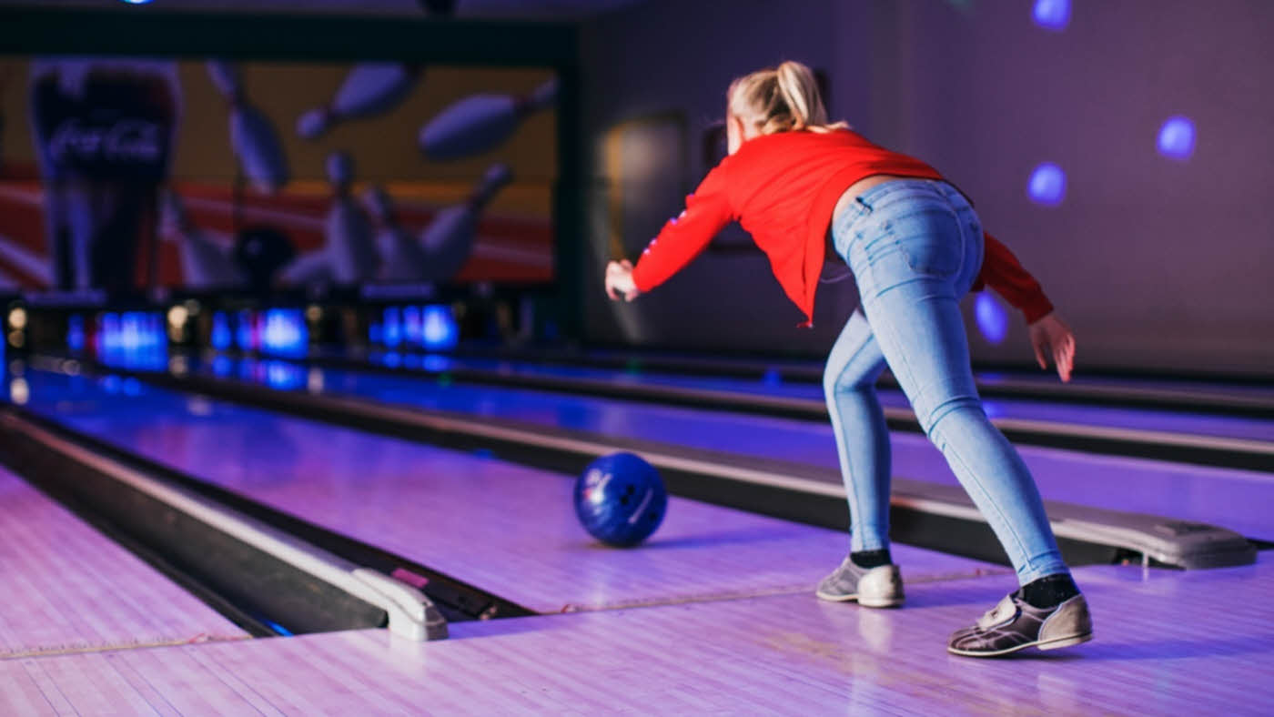 Jente i lyse jeans og rød genser kaster bowlingkule