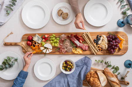 Et bugnende tapasbrett med ost, kjøtt, frukt og nøtter står midt på bordet, omgitt av tallerkener.