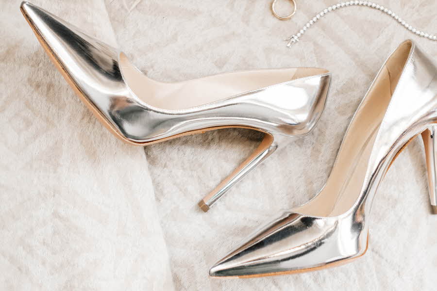 Et par høyhælte sko i sølv på et hvitt teppe.