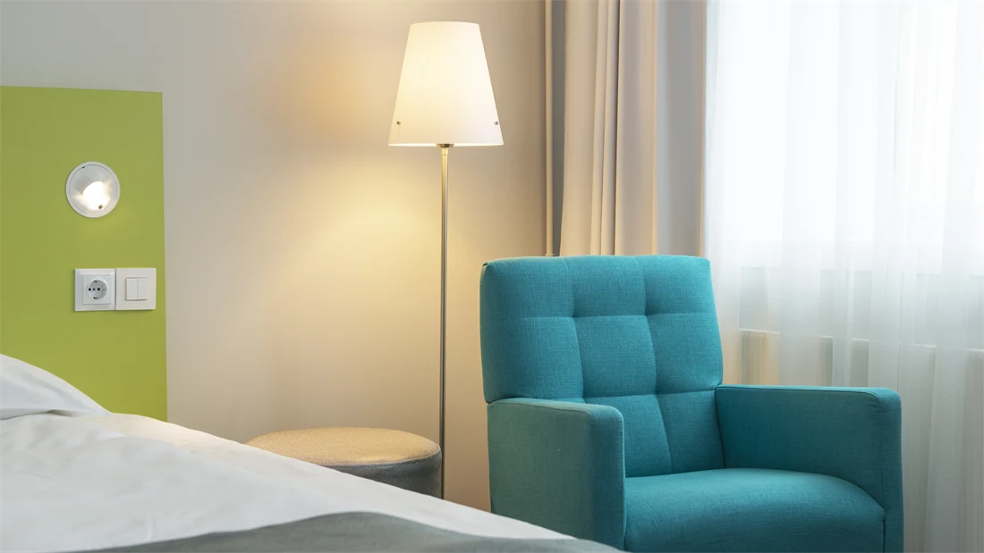 Nærbilde av turkis lenestol og limegrønt sengegavl på Standard Room Queen på Thon Hotel Trondheim. 