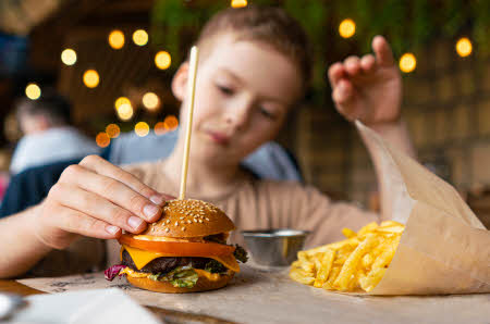 Gutt som skal til å spise en burger. pommes frittes ved siden av