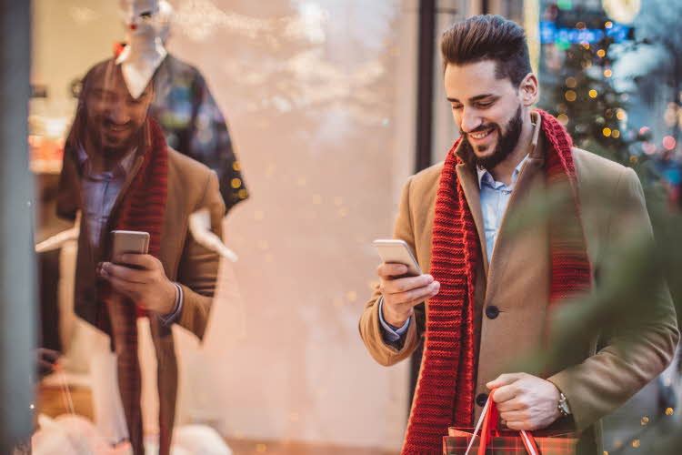 Mann ser på mobilen sin og smiler utenfor butikkvindu i julegate.