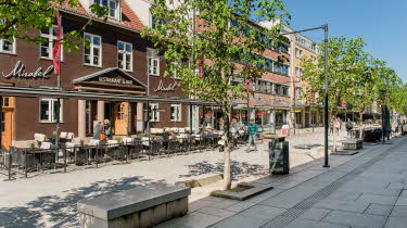 Bildet viser gågata i Lillestrøm med restauranter, butikker, grønne trer og benker.