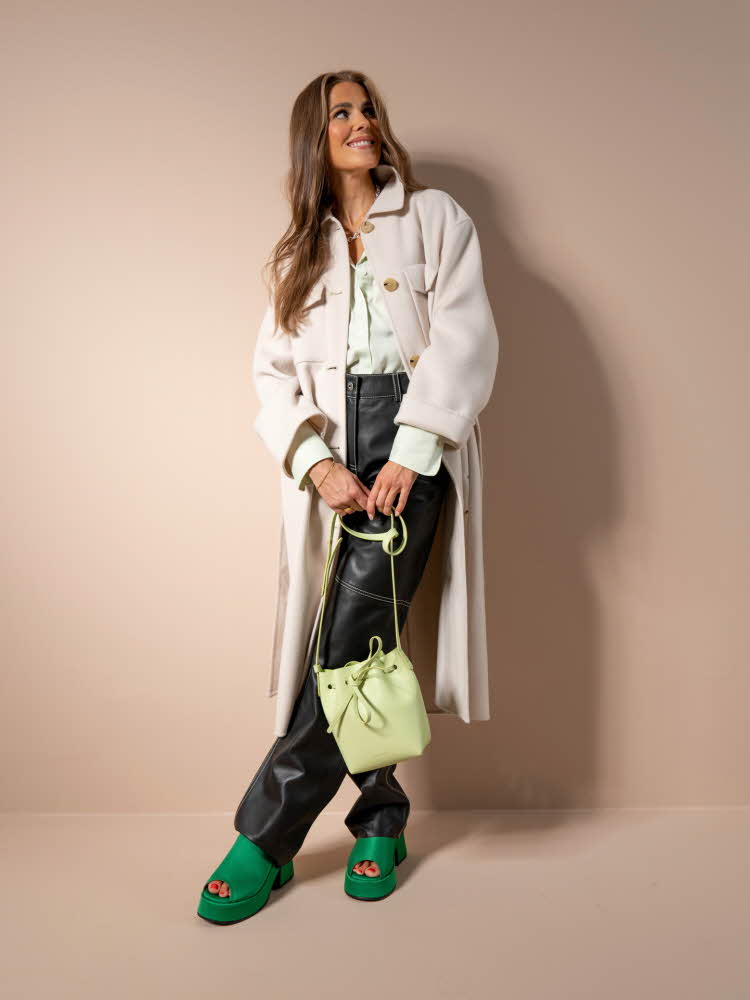 Nina Sandbech med lys beige kåpe, lys skjorte, sort skinnjakke, lys grønn veske og grønne sko