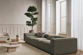 Et moderne og lyst stueinteriør med grønn sofa, grå puter og to kaffebord.
