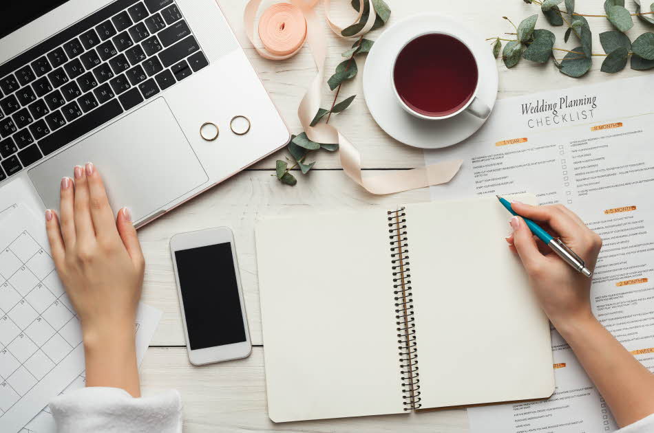 Flat lay av notatbok, mac, te og annet planleggingsutstyr til bryllup