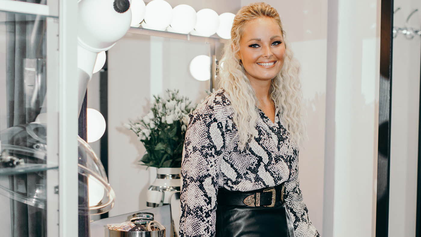 Janne Celin står iført bluse med slangeprint, et skinnskjørt og statement belte