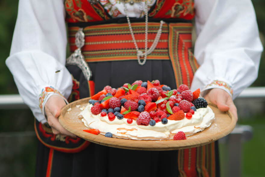 Dame i bunad holder et kakefat med Pavlova fylt med krem og bær