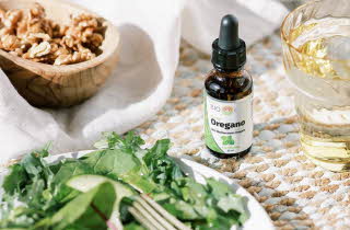 Bio Life Oregano-flaske på et bord med grønnsaker og valnøtter.