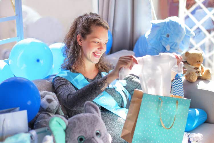 babyshower av dame som sitter i sofa med blå ballonger, bamser og gaver