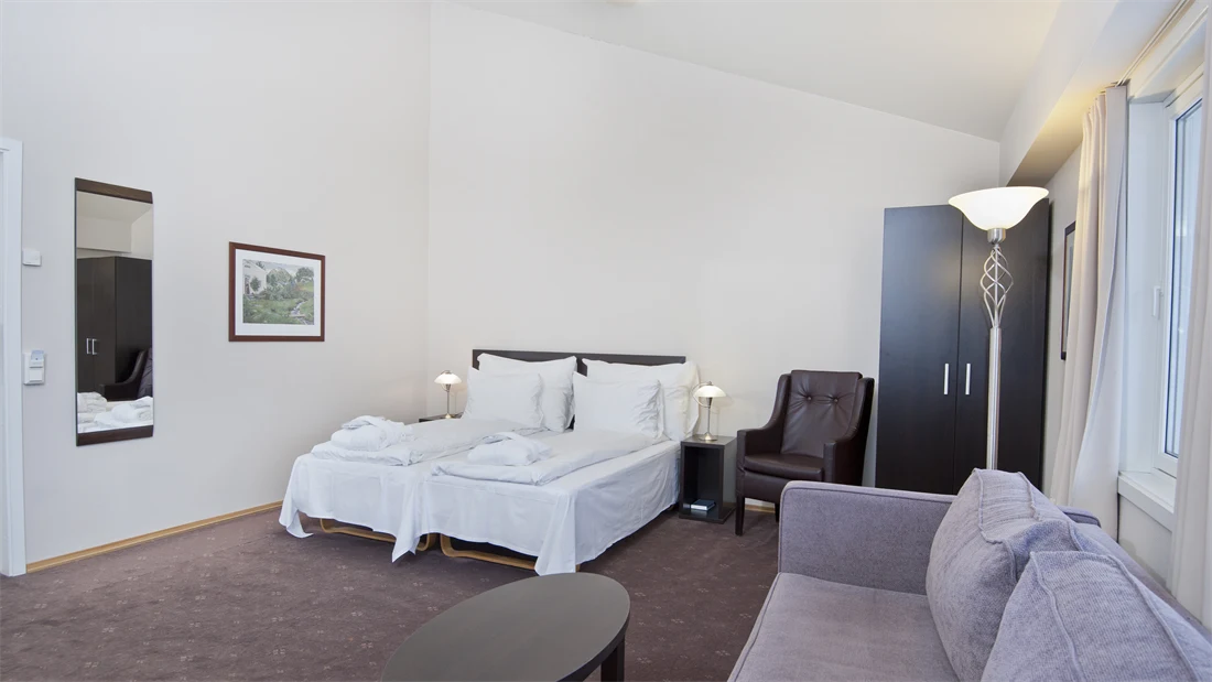 Romslig rom med dobbeltseng, sofa, klesskap og lenestol i superior room på Thon Hotel Jølster, som ligger ved Jølstravatnet - midt mellom Bergen og Ålesund