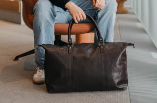 En person som sitter i en stol og holder på en brun bag som står på gulvet