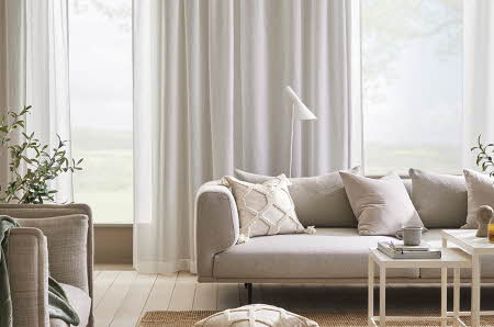 stue med store lye vinduer, lyse gardiner, sofa, pynteputer og stuebord