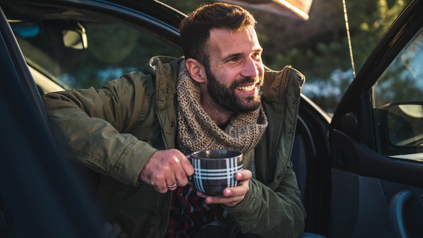 Smilende mann i bil som holder på en kaffekopp