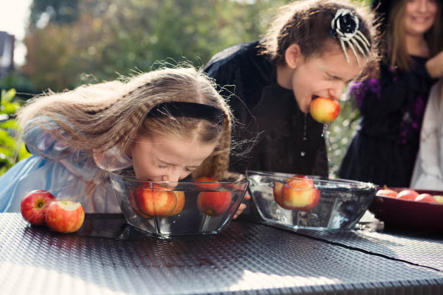 To jenter som spiser epler i en bolle med vann uten å bruke hendene