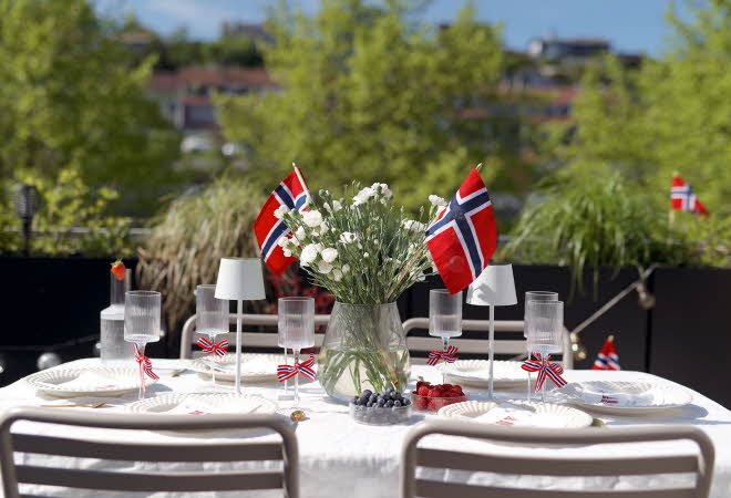 Bord dekket til utendørs måltid med norske flagg og to hvite utelamper.