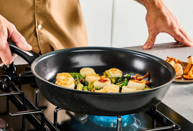 Nærbilde av en person som steker kamskjell i en stekepanne.