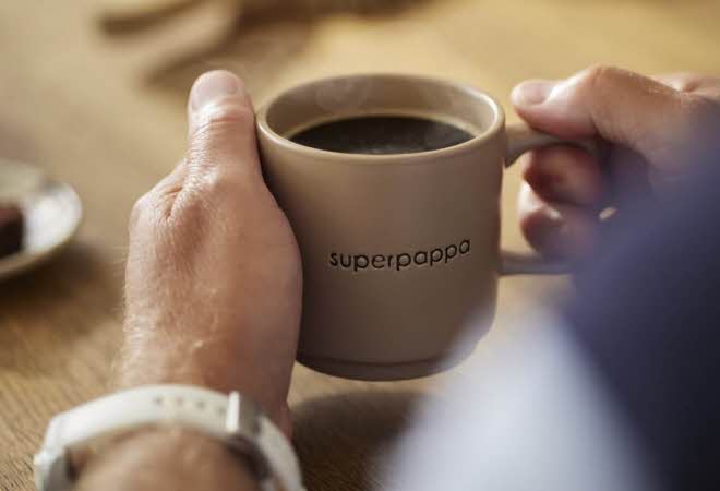 En mann som holder en kopp kaffe med tekst "superpappa" på koppen