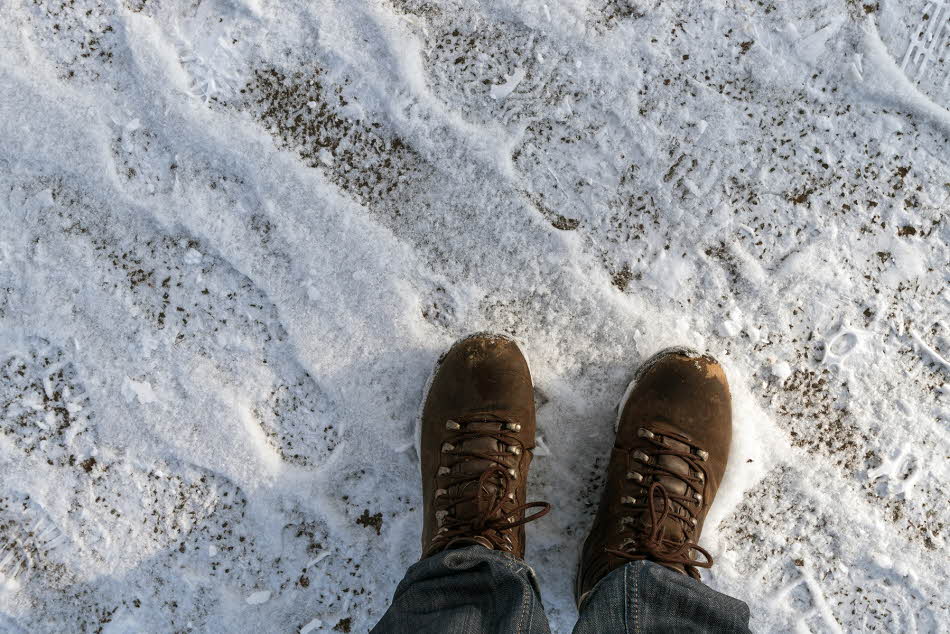 Nærbilde av føtter med snøresko i brunt skinn som står på grus og snø
