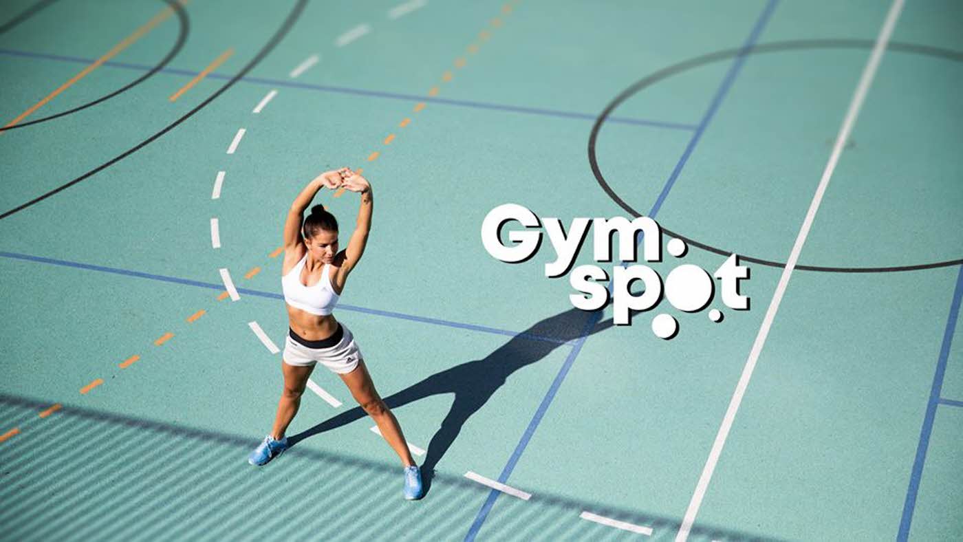 dame strekker armene i en gymsal med turkis gulv