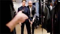 Ansatt i en herreklesbutikk hjelper en kunde med å prøve en dress.