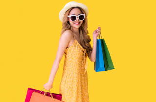 Dame med solbriller, hatt og sommerkjole som holder shoppingposer