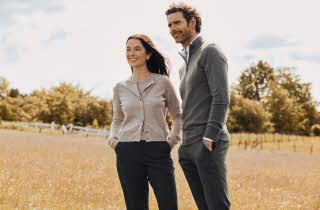 En mann i grå genser og en kvinne i beige cardigan står ute på en åker