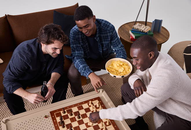 Tre menn som spiller sjakk ved et stuebord.