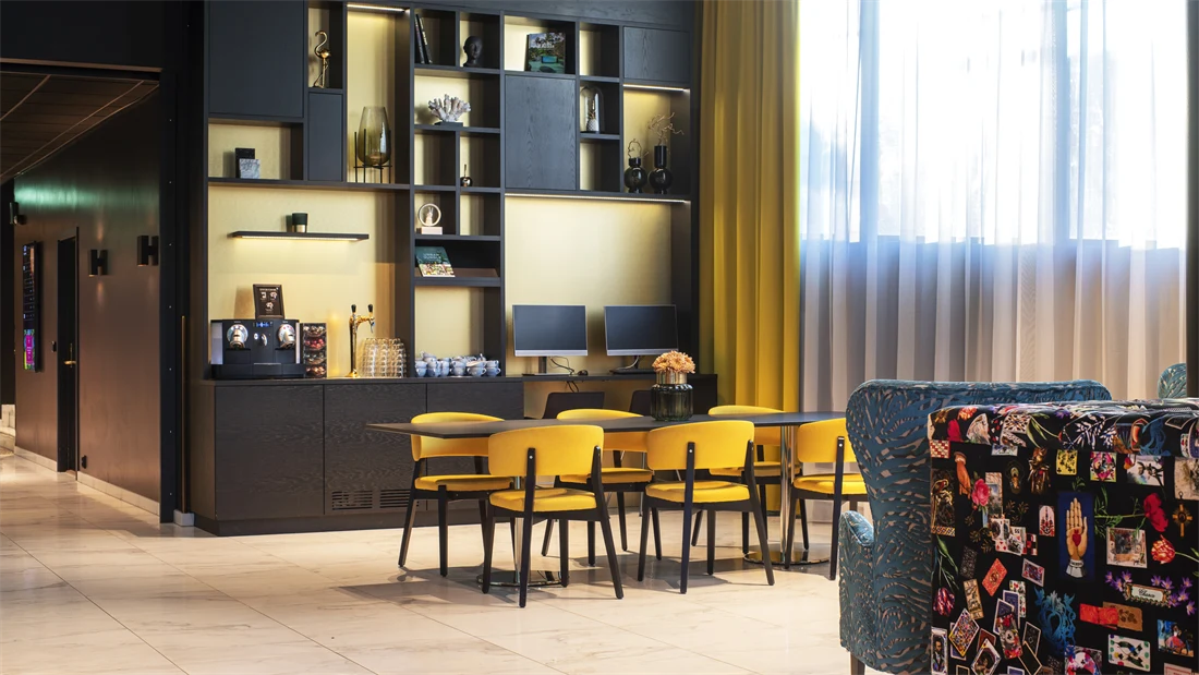 Sort hyllseksjon med kaffemaskin og PCer, sort bord med gule stoler og gule gardiner i resepsjonen på Thon Hotel Storo