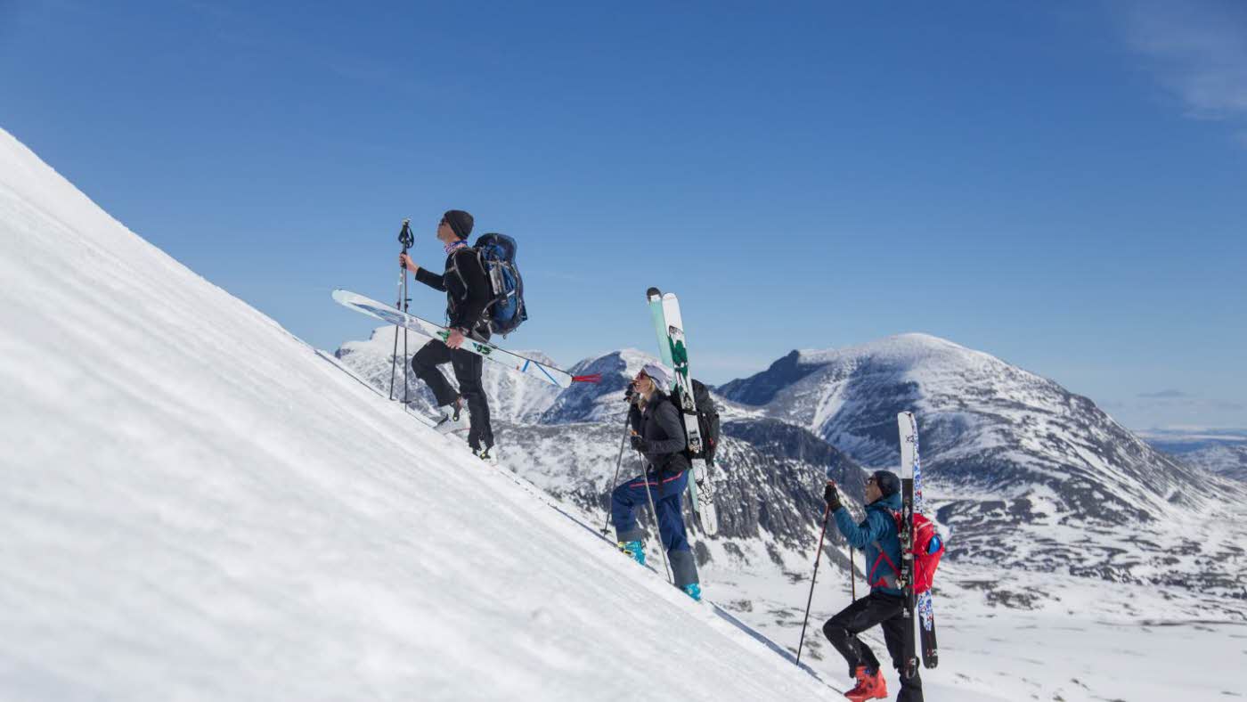tre perosner på topptur i rondane på vei opp ett fjell med ski