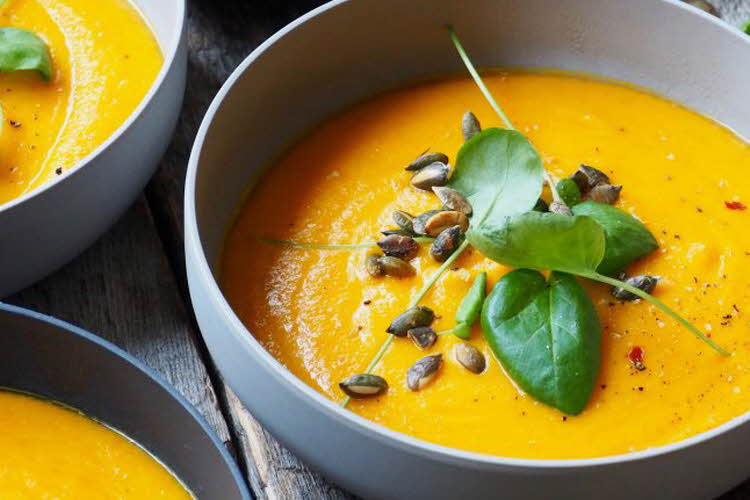 Nærbilde av skåler med gresskarsuppe pyntet med basilikum