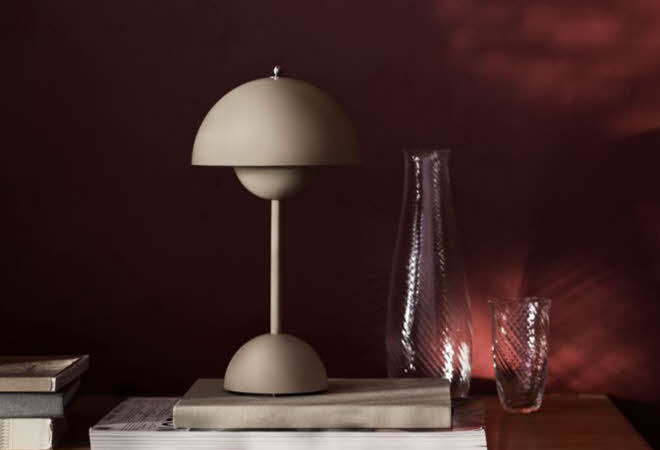 Beige bordlampe med halvkuleformet skjerm står på en stabel bøker ved siden av en glassvase.