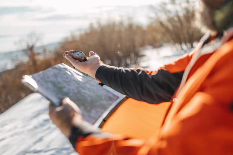 Mann holder kart og kompass i snødekt landskap
