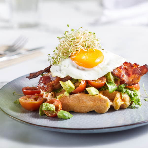 en tallerken med belgisk vaffel, avocado, tomat og egg