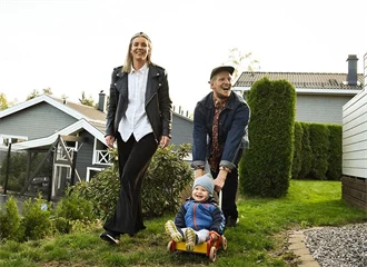 Par med litebarn i en hage med grønt gress og hus i bakgrunnen