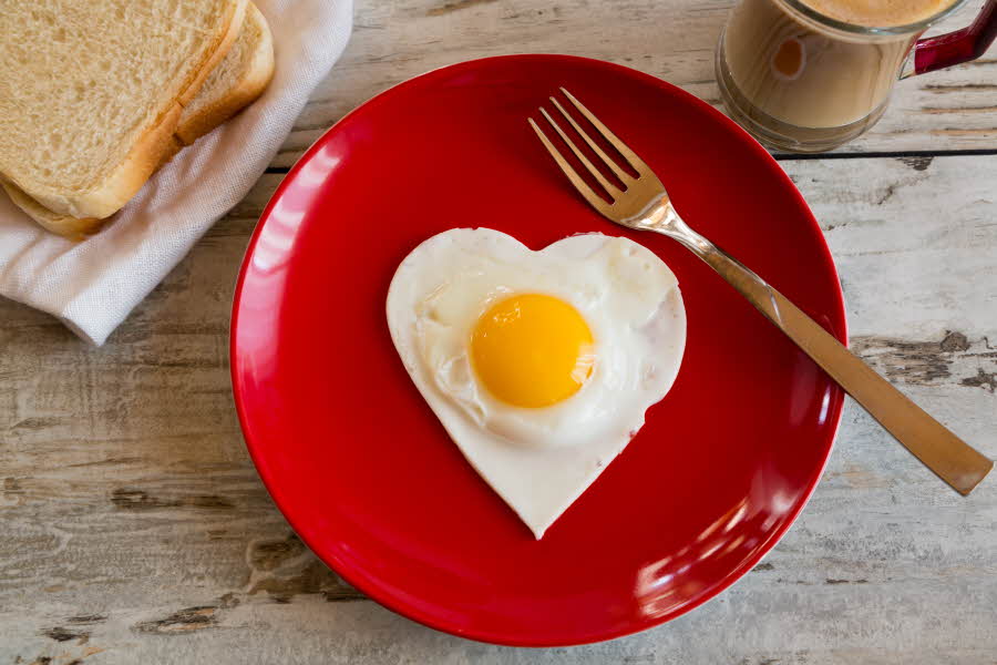hjerteformet speilegg på rødt fat, sammen med en gaffel og med ristet brød og en lattekopp ved siden av