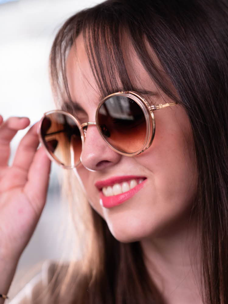 Jente med brunt halvlangt hår og rød leppestift har på seg runde beige solbriller fra Dita