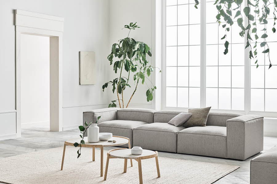 Lys stue med grønne planter, grå sofa og to stuebord