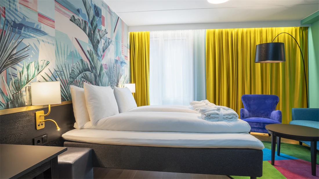 Dobbeltseng, fargerik palmetapet og blå stol i superior HCP rom på Thon Hotel Storo